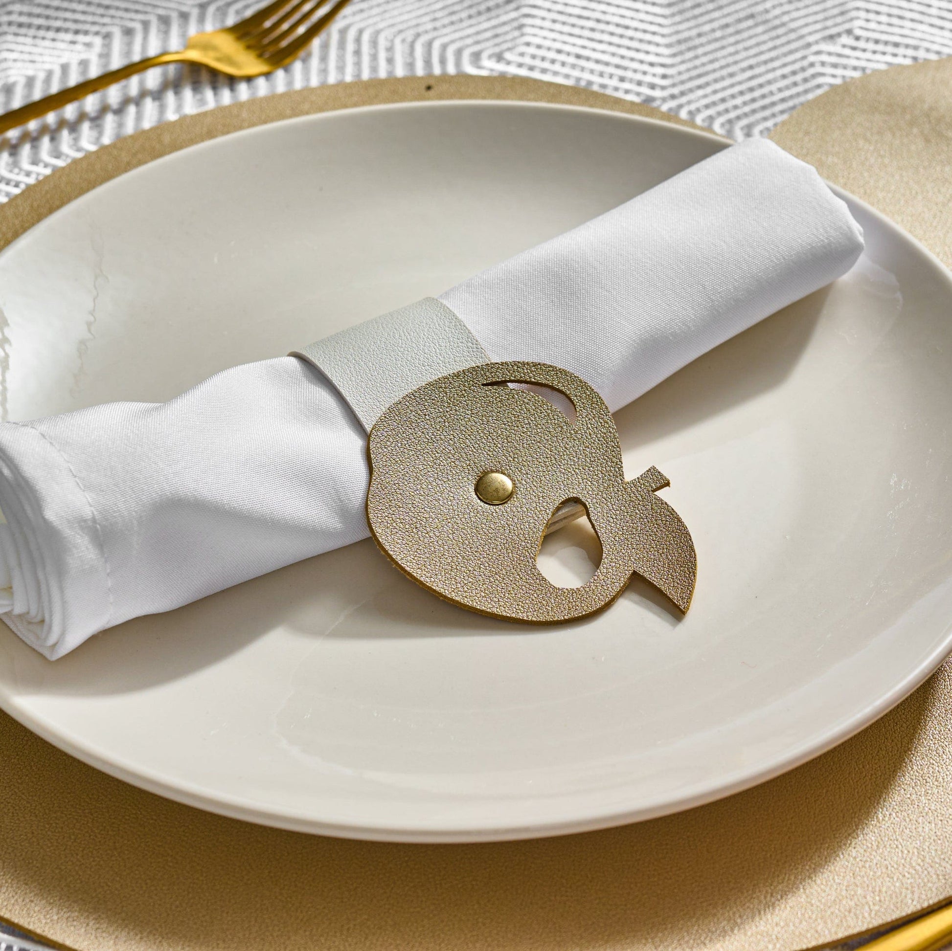 Gold Leather Simanim Napkin Wrap on top of a white plate and Gold leather charger