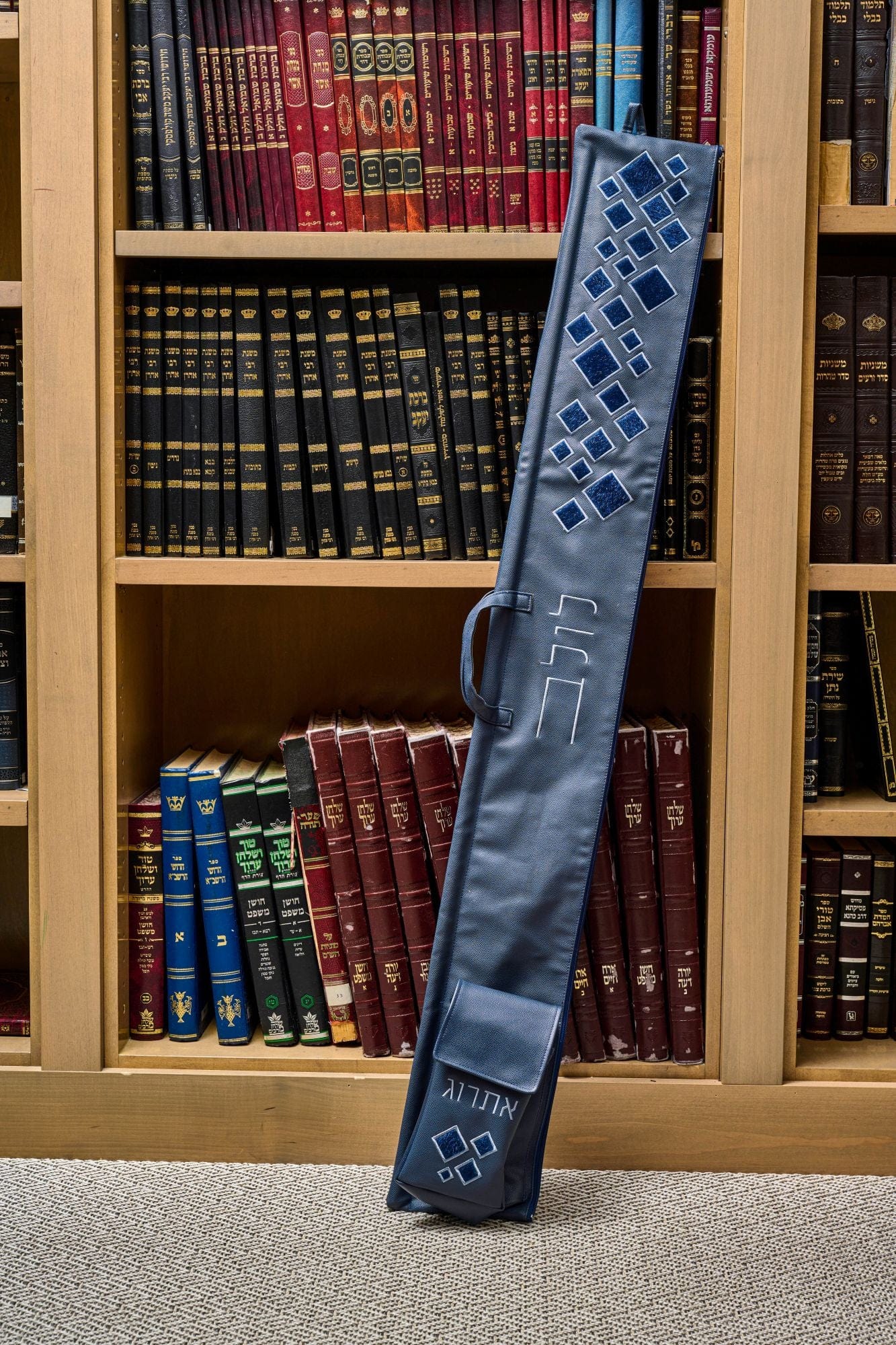 Scattered Fur Lulav and Esrog Case leaning against a wooden bookcase filled with Jewish sefarim.